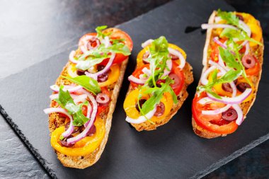 Karanlık bir arka planda İspanyol tapaları. Domates, soğan, yeşillik ve zeytinli vejetaryen tapas. Tahta tahtada sağlıklı sandviçler. Üst görünüm