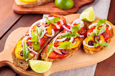 Kesme tahtasında sağlıklı vejetaryen tapas ve limon. Domatesli, yeşillikli ve zeytinli vejetaryen tostları. Tahta tahtalarda sandviçleri aç. Üst görünüm
