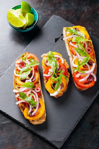 Karanlık bir arka planda İspanyol tapaları. Domates, soğan, yeşillik ve zeytinli vejetaryen tapas. Tahta tahtada sağlıklı sandviçler. Üst görünüm