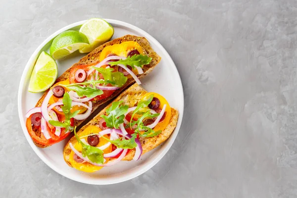 Sağlıklı vejetaryen tostları ve beyaz tabakta limon. Domatesli, yeşillikli ve zeytinli Sağlıklı açık sandviçler. Üst Manzara. Boşluğu kopyala