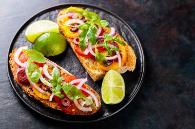 Karanlık bir arka planda vejetaryen sandviçler. Sebzeli İspanyol mezesi, yeşillik, zeytin ve limon. Siyah tabakta sağlıklı sandviçler. Üst Manzara. Boşluğu kopyala