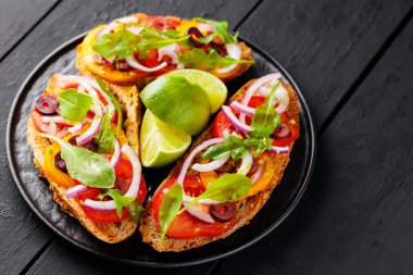 Sağlıklı vejetaryen tostları ve siyah tabakta limon. Domatesli, yeşillikli ve zeytinli Siyah tahtada sağlıklı açık sandviçler. Uzayı kopyala Üst görünüm