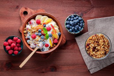 Bowl of homemade granola with yogurt and fresh berries on wooden background. Healthy breakfast with yogurt, granola and fruits on cutting board. Flat lay