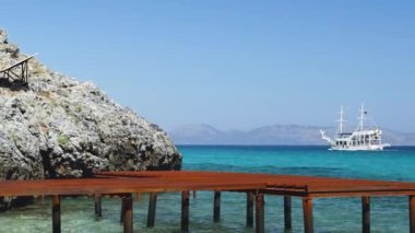 Sea pier and solar panel on the rocks. Pleasure ship sails on the sea of turquoise color. Concept of a sea trip on a ship