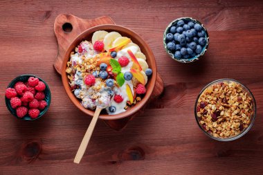Bowl of homemade granola with yogurt and fresh berries on wooden background. Healthy breakfast with yogurt, granola and fruits on cutting board. Flat lay