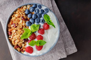 Healthy breakfast with homemade granola, yogurt, blueberry and raspberry. Greek yogurt with granola, berries and mint in a gray bowl. Top view. Copy space
