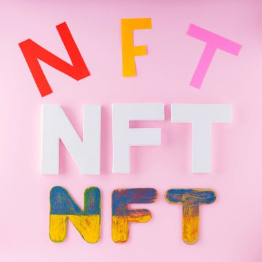 NFT inscriptions on pink background.  Non-Fungible Token folded with multi-colored letters. Crypto art concept. Top view