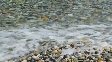 Sea water waves polishing pebbles and stones. Coastline with pebble beaches and clear water surface