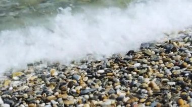 Sea water waves polishing pebbles and stones. Coastline with pebble beaches and clear water surface