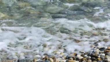Sea water waves polishing pebbles and stones. Coastline with pebble beaches and clear water surface