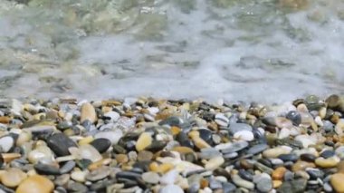Sea water waves polishing pebbles and stones. Coastline with pebble beaches and clear water surface