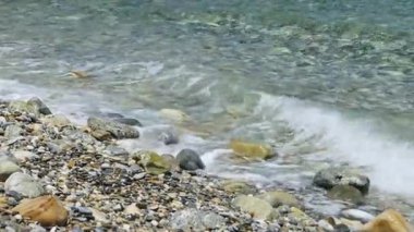 Waves on a pebble beach and a metal pier. Seashore on a sunny day. Sea tourism concept