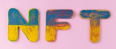 NFT inscription with blue-yellow wooden letters. Non-fungible token on a pink background. Crypto Art concept