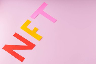 Non-fungible token inscription from paper letters. NFT on a pink background. Concept of crypto art and blockchain technology. Copy space