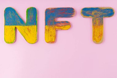 Pembe arka planda ödenmeyen jeton. Mavi-sarı ahşap harfli NFT yazıtları. Boşluğu kopyala