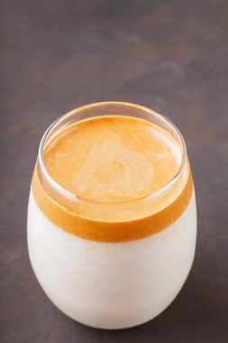 Korean iced Dalgona coffee in glass on a dark background. Dalgona coffee in a transparent glass close-up. New popular drink trend