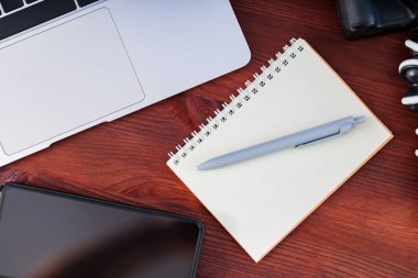 Freelancer 'ın işyeri. Laptop, akıllı telefon ve defter tahta bir masanın üzerinde. Ev idaresi ve uzaktan çalışma kavramı. Üst görünüm