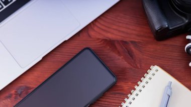 Freelancer 'ın işyeri. Laptop, akıllı telefon ve defter tahta bir masanın üzerinde. Ev idaresi ve uzaktan çalışma kavramı. Üst görünüm