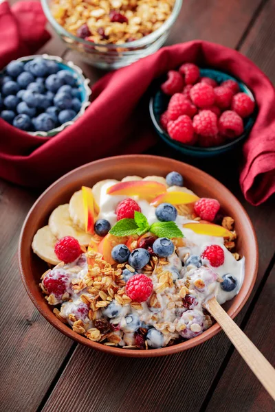 Greek yogurt with granola, berries and fruits on a wooden table. Healthy breakfast with granola, yogurt and fruits on a clay plate with a wooden spoon. Top view