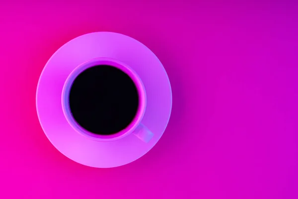 Cup of coffee and saucer in pink neon light. Coffee on a creative pink background. Top view. Copy space