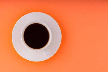 Turuncu arka planda bir fincan kahve. Beyaz bir fincan üzerinde bir fincan sade kahve. Uzayı kopyala Üst görünüm