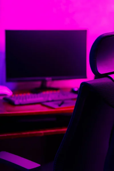 Creative designer\'s workplace, back view. Office chair and work desk view with graphic tablet, computer and smartphone. Retoucher home office in neon pink blue