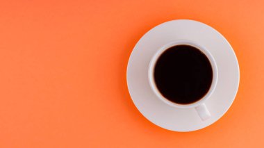 Turuncu arka planda bir fincan kahve. Beyaz bir fincan üzerinde bir fincan sade kahve. Uzayı kopyala Üst görünüm