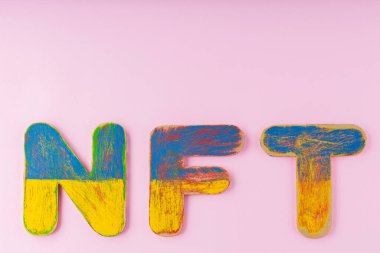 Pembe arka planda ödenmeyen jeton. Mavi-sarı ahşap harfli NFT yazıtları. Boşluğu kopyala