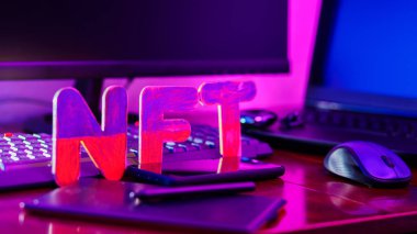 NFT 'nin yaratıcısı dijital bir sanatçı. İş yerinde grafiksel tablet, kalem, akıllı telefon ve bilgisayar donanımlı NFT harfleri var. Neon ışıkta kripto sanat kavramı