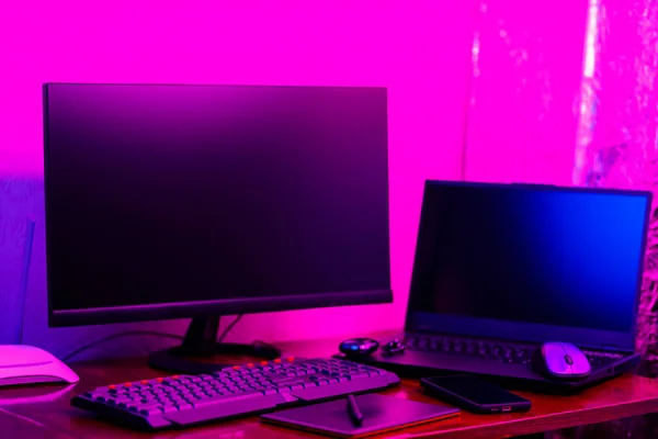 Workplace of a graphic designer and creative retoucher. Graphic tablet, smartphone and computer equipment in neon light. Workspace of creative designer with tablet and stylus