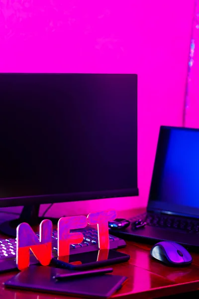 NFT creation by a digital artist in a home office. NFT lettering at workplace with graphics tablet, pen, smartphone and computer equipment. Crypto art concept in neon light