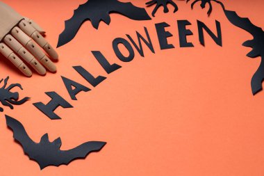 Yapay kollu Cadılar Bayramı konsepti, turuncu arka planda yarasalar ve örümcekler. Ahşap bir el ve yarasa figürleriyle Cadılar Bayramı harfleri. Boşluğu kopyala