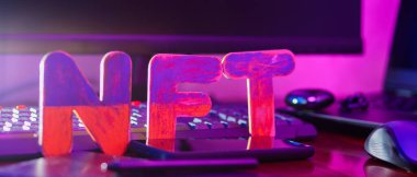 NFT 'nin yaratıcısı dijital bir sanatçı. İş yerinde grafiksel tablet, kalem, akıllı telefon ve bilgisayar donanımlı NFT harfleri var. Neon ışıkta kripto sanat kavramı