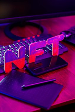 NFT 'nin yaratıcısı dijital bir sanatçı. İş yerinde grafiksel tablet, kalem, akıllı telefon ve bilgisayar donanımlı NFT harfleri var. Neon ışıkta kripto sanat kavramı