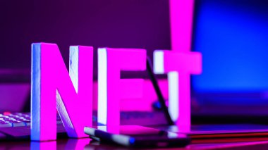 3 boyutlu bir yazıcıya basılmış 3 boyutlu harflerden yapılmış NFT yazıtları. İş yerinde grafiksel tablet, akıllı telefon ve bilgisayar donanımlı NFT harfleri var. Pembe-mavi ışıkta iadesi mümkün olmayan jeton.