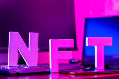 3 boyutlu bir yazıcıya basılmış 3 boyutlu harflerden yapılmış NFT yazıtları. İş yerinde grafiksel tablet, akıllı telefon ve bilgisayar donanımlı NFT harfleri var. Pembe-mavi ışıkta iadesi mümkün olmayan jeton.