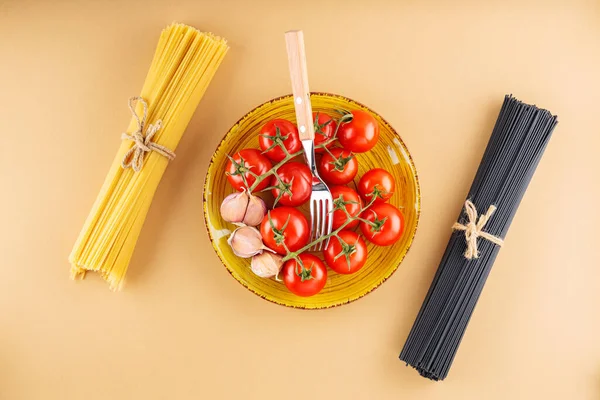 生の黒と黄色のスパゲティトマトとニンニクベージュの背景に パスタと黄色のプレート上の新鮮な野菜 トップ表示 — ストック写真