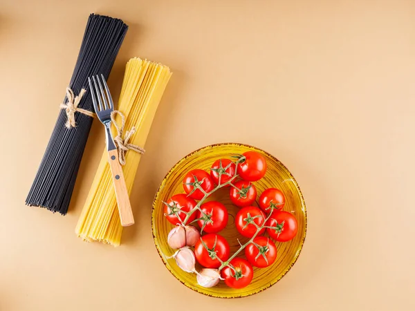 生の黒と黄色のスパゲティトマトとニンニクベージュの背景に パスタと黄色のプレート上の新鮮な野菜 トップ表示 — ストック写真
