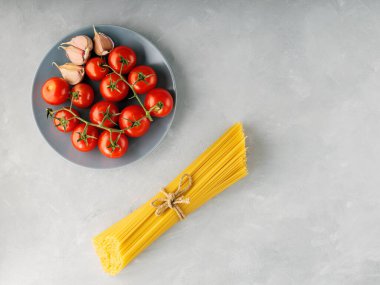 Domatesli makarna ve gri arka planda sarımsak. İtalyan makarnası için sicim ve malzemelerle bağlanmış bir demet spagetti. Üst Manzara. Boşluğu kopyala