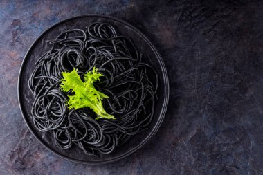 Siyah arkaplanda mürekkep balığı mürekkebi olan siyah spagetti. Yeşil marullu siyah spagetti makarna. Üst Manzara. Boşluğu kopyala
