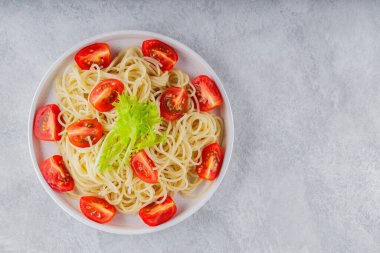 Beyaz tabakta taze vişneli domatesli spagetti pişirdim. Gri arka planda sebzeli spagetti makarna. Üst Manzara. Boşluğu kopyala