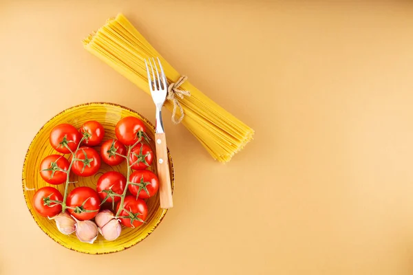 ベージュの背景にトマトとニンニクとパスタスパゲティ 生パスタと新鮮な野菜 最上階だ スペースのコピー — ストック写真