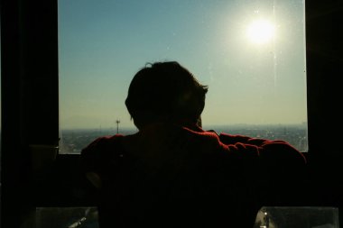 Pencerenin arkasında sırt çantası olan kırmızı elbiseli bir adamın silueti.