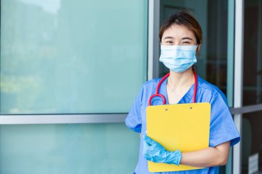 Asyalı hemşire sağlık görevlilerinin portresi hastanede yüz maskesi ile duruyor ve mesaj için yer var..