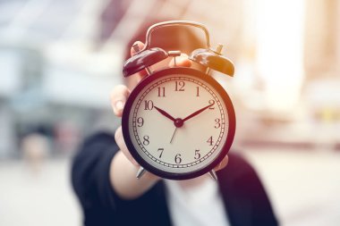 Kapatma işi yapanlar, ellerinde alarmlı saat, açık hava bulanık ofis arka planı tutuyorlar.