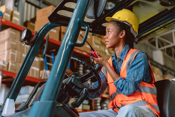 African black woman cargo worker work in warehouse working staff forklift driver command loading with ham radio.