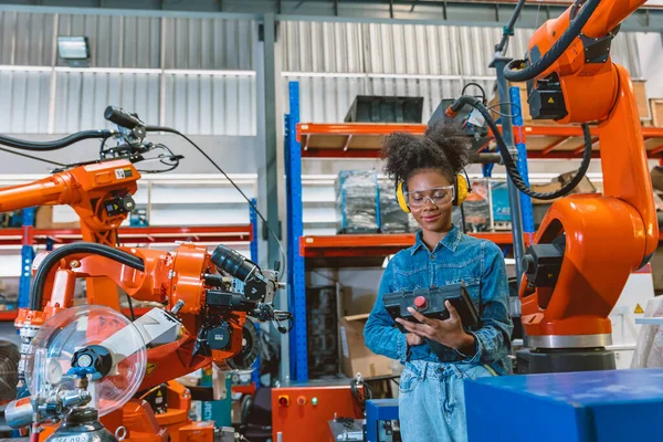 Engineer smart woman worker working programing robotic welding machine. Black teen girl work in advance modern factory.