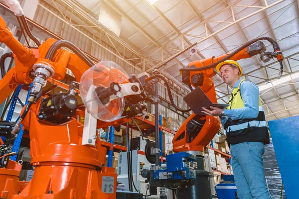 Worker man working with robot arm automate welding machine in modern metal factory. Engineer program robotic in heavy industry.