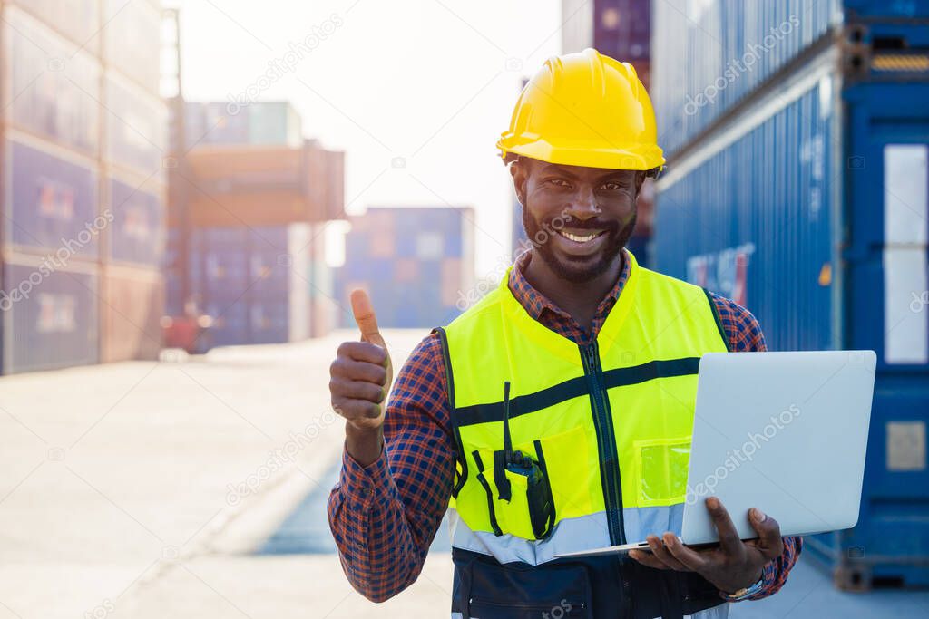 Portrait Black African staff worker happy smile working in cargo crane shipping logistic port with laptop computer.