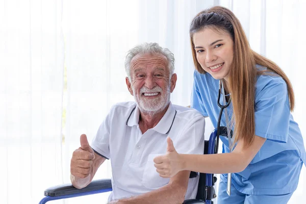 closeup healthy senior elder man with doctor nurse at homecare thumbs up happy smile